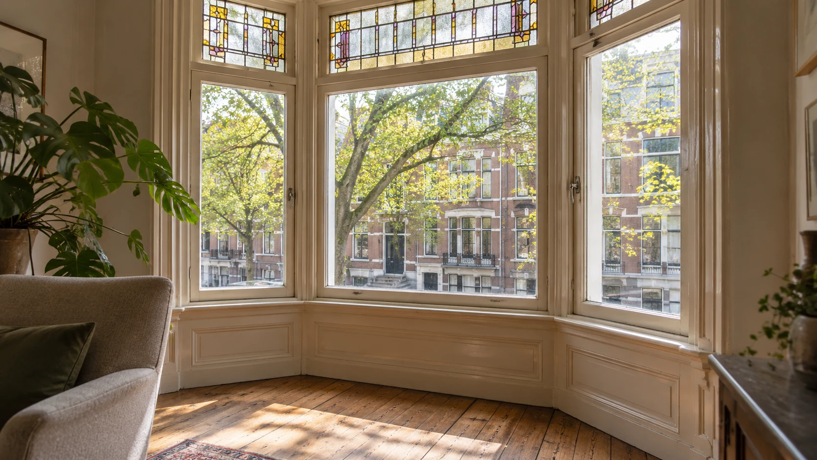 Sfeerbeeld van een erker met glas-in-lood en uitzicht op een groene Rotterdamse straat